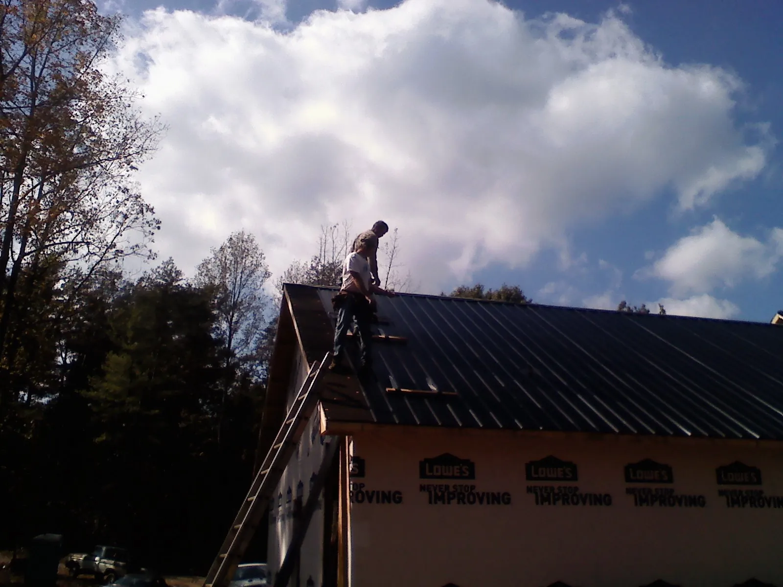 Roofer fastening dark metal panels high against a cloudy sky, from a Roof Inspection job in Edgefield