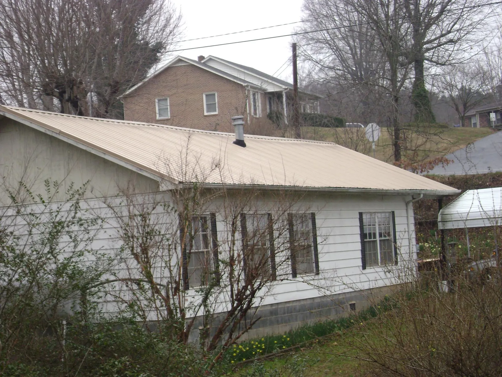 Tan metal roof on a white sided house set into a hillside — Commercial Roofing by Roofing Brothers in Edgefield